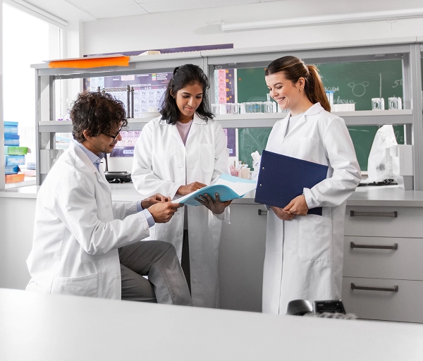Scientists in laboratory examining cell cultures under microscope with bioreactor equipment visible in background.